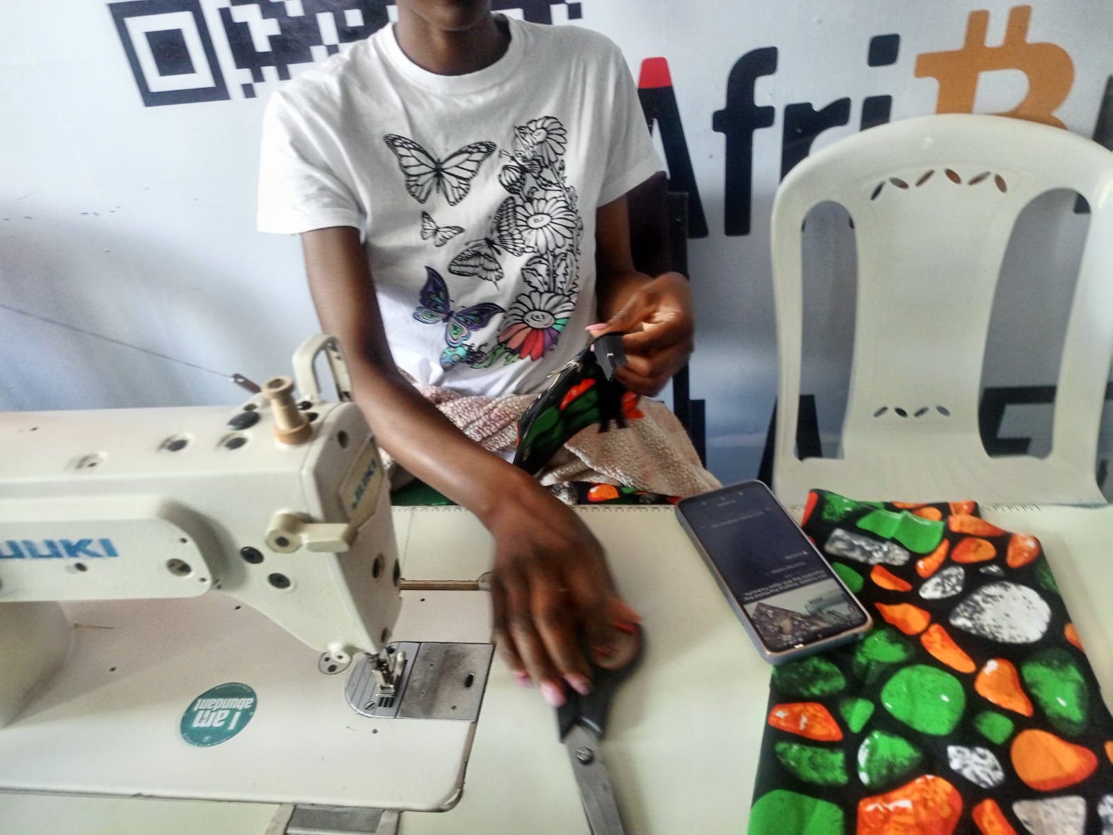 Hands using scissors and patterned fabric at a sewing workstation in Kenya.